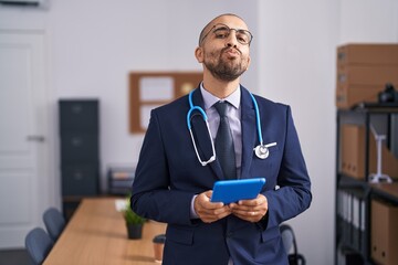 Hispanic man with beard wearing doctor stethoscope working at the office looking at the camera...