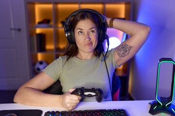 Beautiful brunette woman playing video games wearing headphones confuse and wondering about...