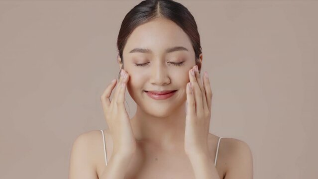 Young beautiful Asian woman demonstrate moisturizing facial care touching cheek and massages her face gently with fingertips.
