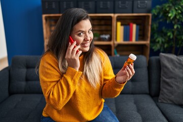 Young beautiful plus size woman talking on smartphone holding pills at home