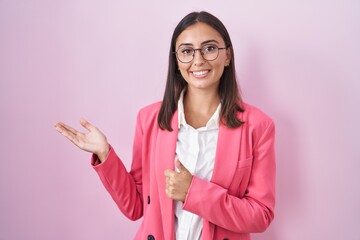 Young hispanic woman wearing business clothes and glasses showing palm hand and doing ok gesture with thumbs up, smiling happy and cheerful