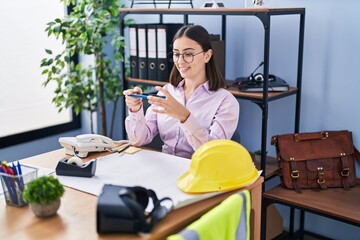 Young hispanic woman architect make photo by the smartphone to plans at office