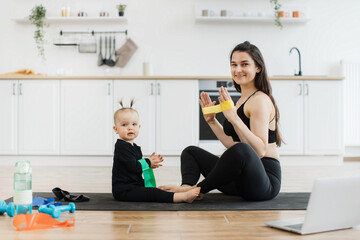 Beautiful lady and adorable child sitting with soles of feet together on floor while having fun...