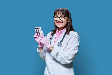 Woman doctor showing pills in blister, blue studio background