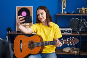 Fototapeta na wymiar Young woman musician make selfie by smartphone holding classical guitar at music studio