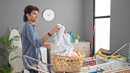 Young hispanic man hanging clothes on clothesline at laundry room