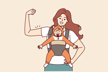 Strong mother with newborn in baby carrier shows biceps demonstrating confidence in happy future of child. Young self-confident mother proud to raise son or daughter alone for feminism concept