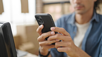 Young hispanic man ecommerce business worker using smartphone sitting on table at office