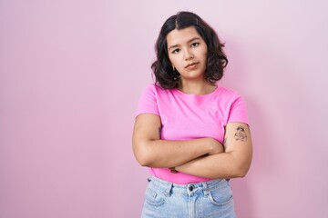Young hispanic woman standing over pink background skeptic and nervous, disapproving expression on...