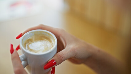 Young blonde woman holding cup of coffee sitting on table at coffee shop