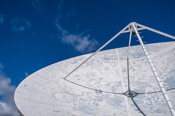 Detail of the interior of a large satellite dish for stargazing, decorated as if it were the surface of the moon, with the craters in blue and white, with large white clouds in the background. Museum 