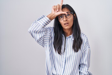 Naklejka premium Young hispanic woman wearing glasses making fun of people with fingers on forehead doing loser gesture mocking and insulting.