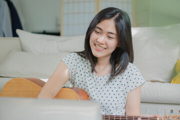 Attractive Asian female is learning online guitar course by using laptop or watch and practice...