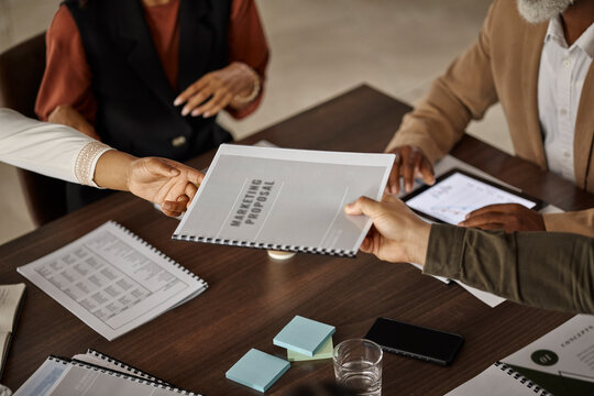 Documents, proposal or hands of business people in a meeting planning a financial strategy together. Data analytics, teamwork or manager giving worker a marketing portfolio report file or paperwork