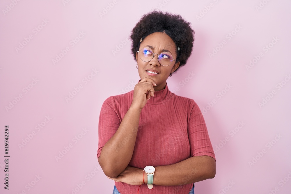 Sticker Beautiful african woman with curly hair standing over pink background thinking worried about a question, concerned and nervous with hand on chin