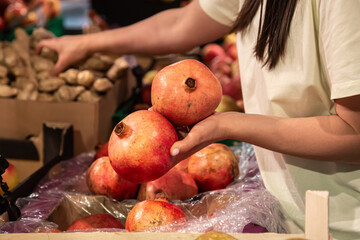 The woman holds pomegranate in the store or in the market, close up.