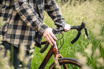 A man holds a bicycle handlebar and walks in the forest, close-up.
