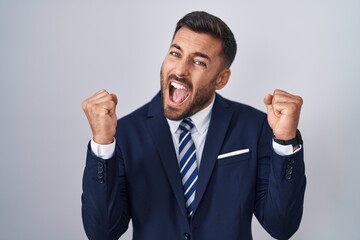 Handsome hispanic man wearing suit and tie celebrating surprised and amazed for success with arms raised and eyes closed. winner concept.