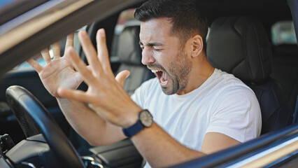 Fototapeta na wymiar Young hispanic man stressed driving car screaming at street