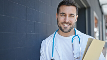 Young hispanic man doctor smiling confident holding medical report at hospital