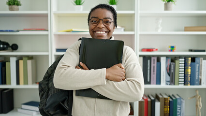 African american woman student wearing backpack holding binder at library university