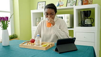 African american woman having breakfast using touchpad at dinning room