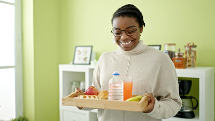 African american woman smiling confident holding breakfast tray at dinning room
