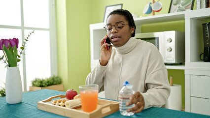 African american woman having breakfast talking on smartphone at dinning room