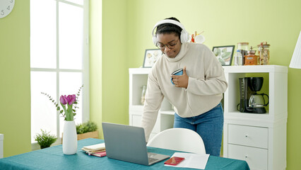 African american woman listening to music holding cup of coffee at dinning room