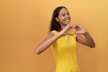 Young african american woman smiling confident doing heart gesture with hands over isolated yellow background