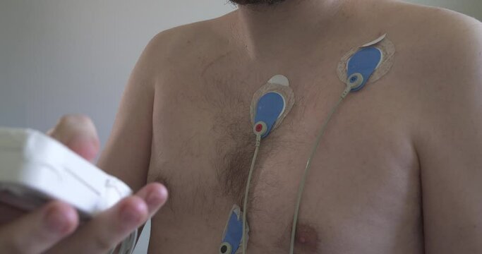Close up shot of young man using heart monitor with electrodes attached to chest