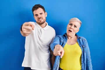 Young brazilian mother and son standing over blue background pointing displeased and frustrated to the camera, angry and furious with you