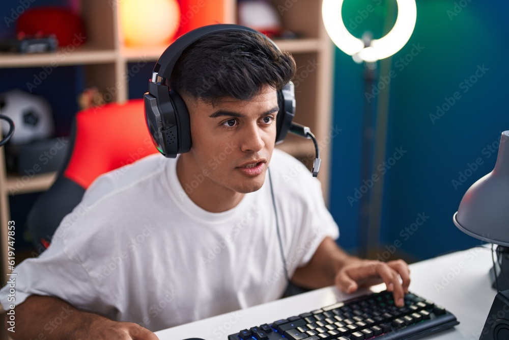 Poster young hispanic man streamer playing video game using computer at gaming room