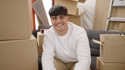 Fototapeta na wymiar Young hispanic man smiling confident sitting on sofa at new home