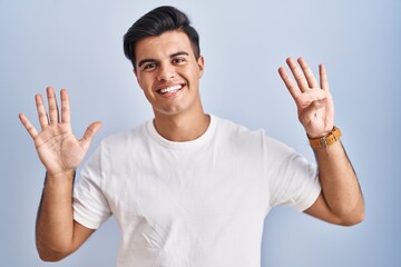 Hispanic man standing over blue background showing and pointing up with fingers number nine while smiling confident and happy.