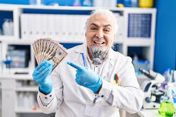 Middle age man with grey hair working at scientist laboratory holding money smiling happy pointing with hand and finger