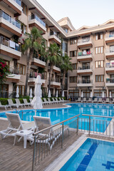 Luxurious hotel with swimming pool, palm trees, sun loungers and seating area. Palm trees are...
