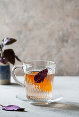 Healthy and immune boosty purple basil tea in a glass mug with slice of orange and fresh leaves backside. Grey concrete background, vertical banner with space for text