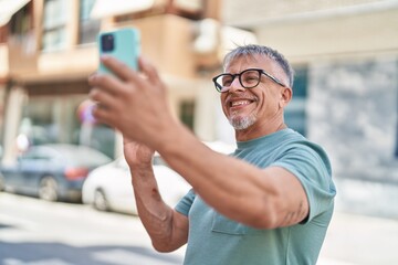 Middle age grey-haired man smiling confident having video call at street