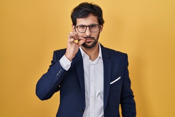 Handsome latin man standing over yellow background mouth and lips shut as zip with fingers. secret and silent, taboo talking