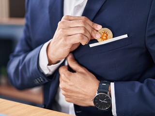 Young hispanic man business worker insert bitcoin on jacket at office
