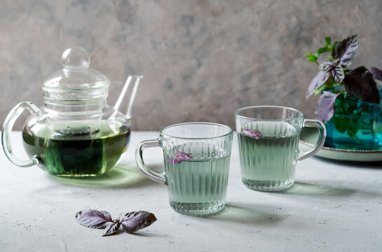 Healthy and immune boosty purple basil tea in a glass mugs and teapot with fresh basil leaves. Grey concrete background