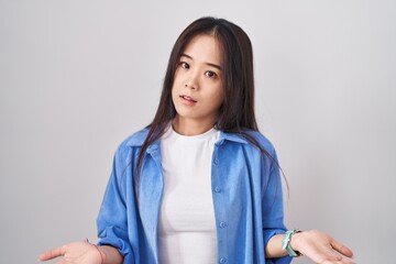 Young chinese woman standing over white background clueless and confused with open arms, no idea concept.