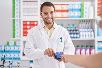 Young man pharmacist using credit card and dataphone at pharmacy