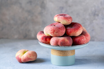 Flat or donut peaches in green grey ceramic cake stand on grey concrete background, place for text
