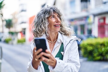 Middle age woman smiling confident using smartphone at street