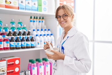 Young blonde girl pharmacist smiling confident working at pharmacy