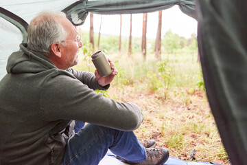 Elderly man having tea while sitting in tent