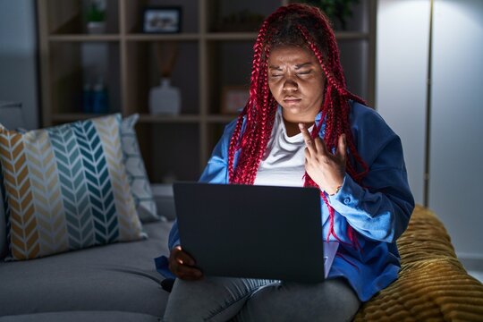 African american woman with braided hair using computer laptop at night showing middle finger, impolite and rude fuck off expression