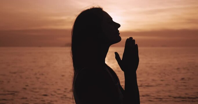 Silhouette young woman praying at sea sunset. Female prayer in religion. Concept of true Faith in God. Religion, spiritual and hope concept. Pray to God.